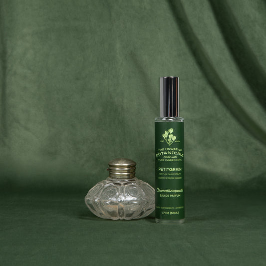 Petitgrain ritual spray beside a cut-glass perfume bottle on a deep green backdrop